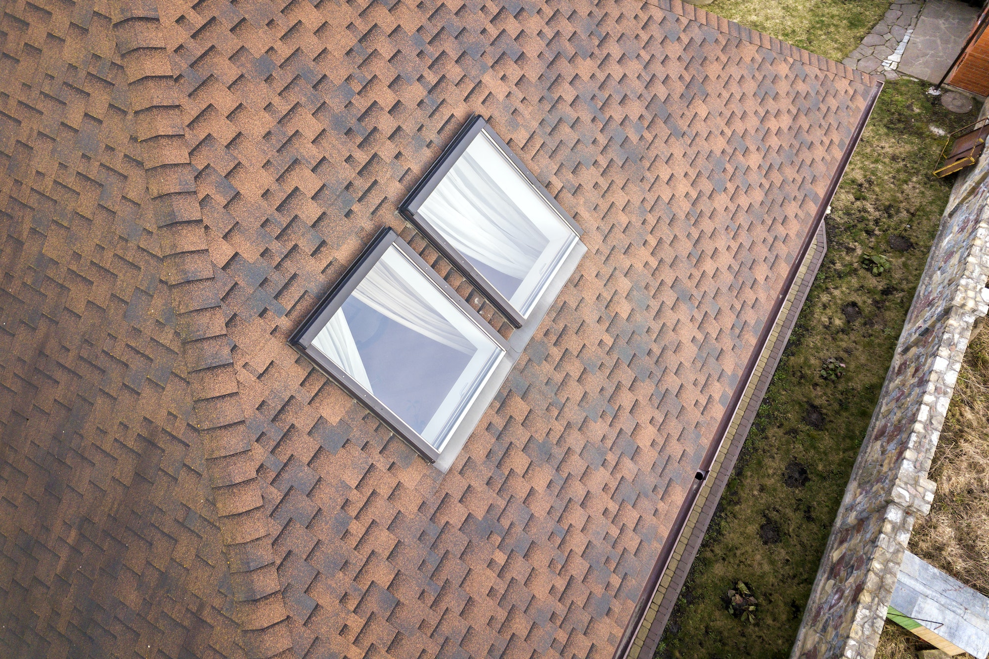 Close-up of new small attic plastic windows installed in brown shingled house roof.